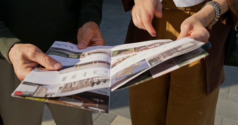 Two people examining a real estate brochure outdoors, possibly discussing design details.