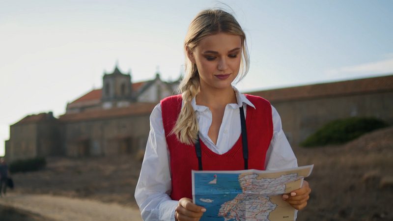 Woman reading a folded travel map in a historical outdoor location under clear sky.