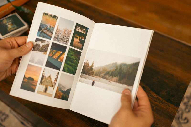 Hands flipping through a printed travel photo book with images of scenic locations.