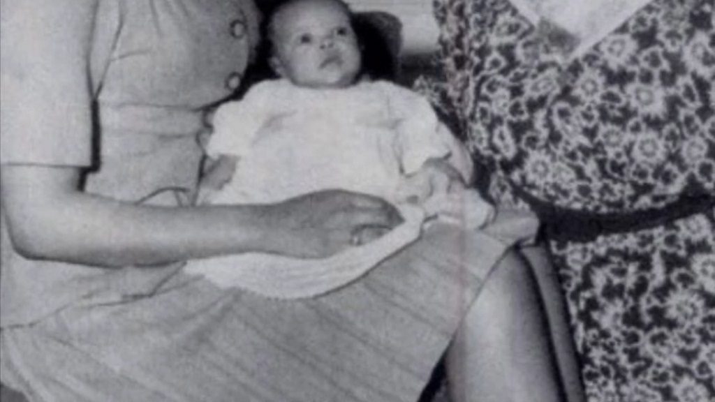 Black and white photo of baby Harolyn Suzanne Nicholas in a white dress, resting in the lap of an adult