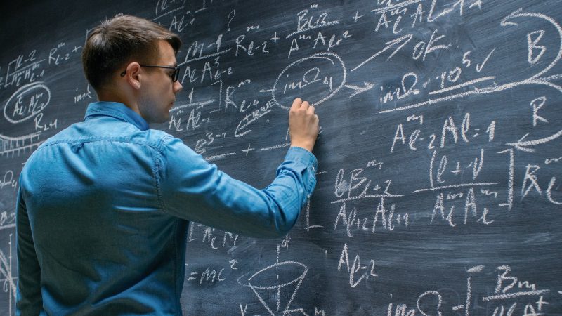 Student writes complex physics equations on a chalkboard
