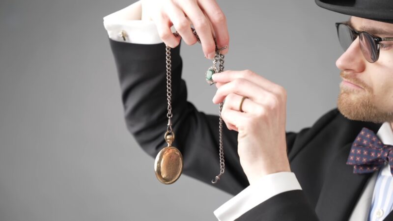 Man holding a vintage pocket watch and chain from a classic gentleman’s accessory kit